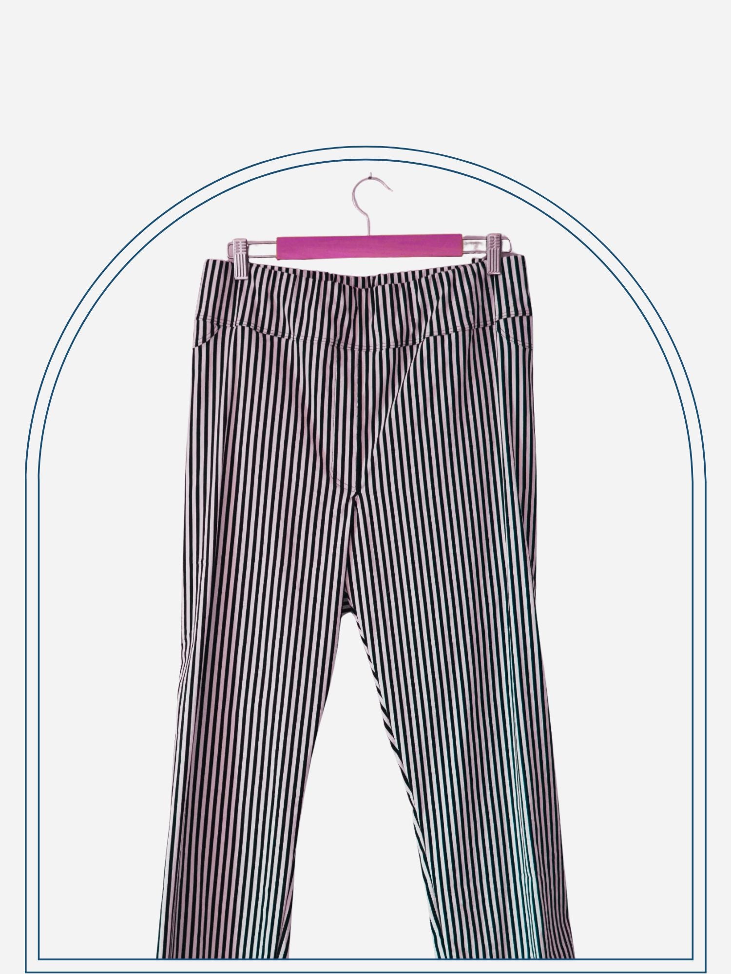 A pair of striped stretch jeans hanging on a wooden hanger against a white wall.