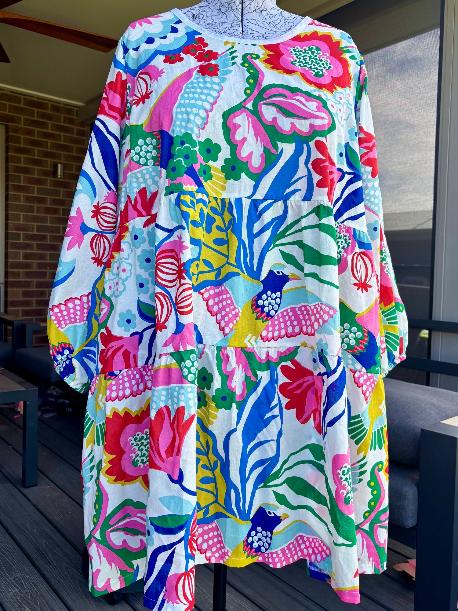 A floral tiered dress displayed on a mannequin, with pockets, against an outdoor background.