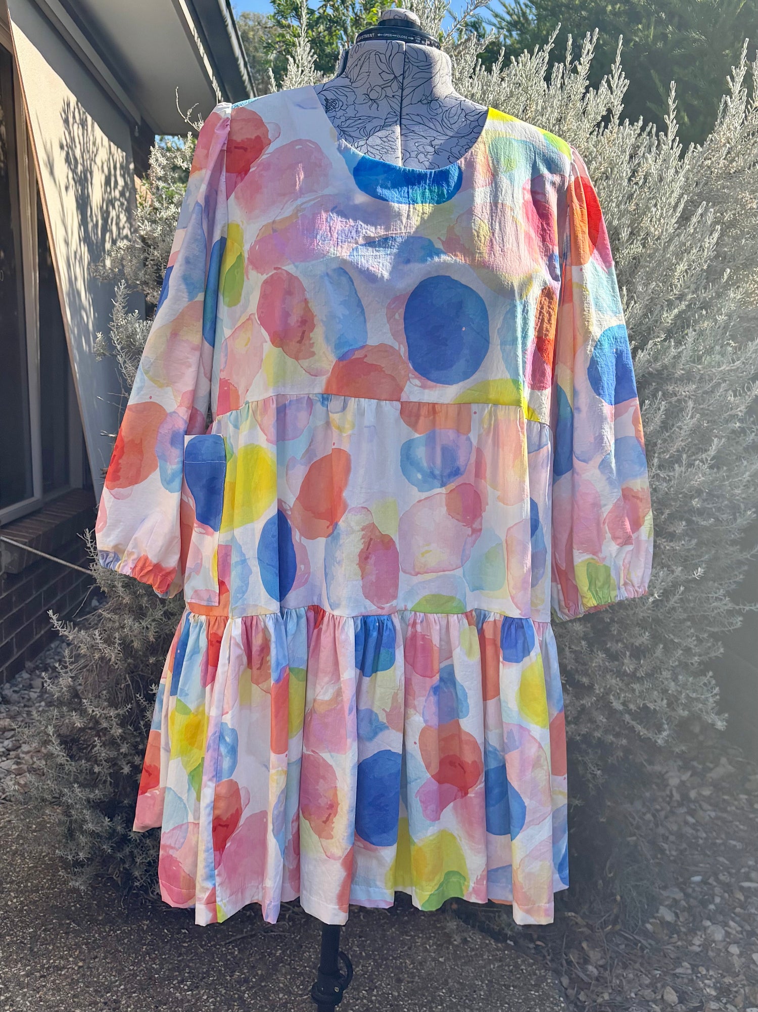 A bubble patterned tiered dress displayed on a mannequin, with pockets, against an outdoor background.