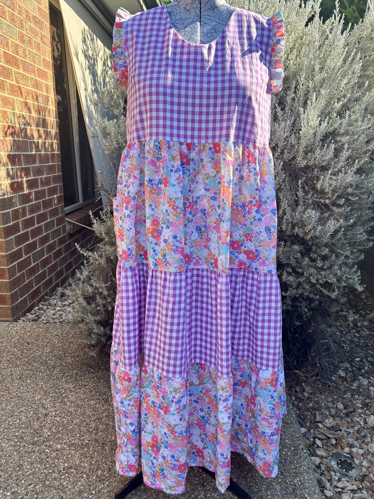 A floral tiered dress displayed on a mannequin, with pockets, against an outdoor background.