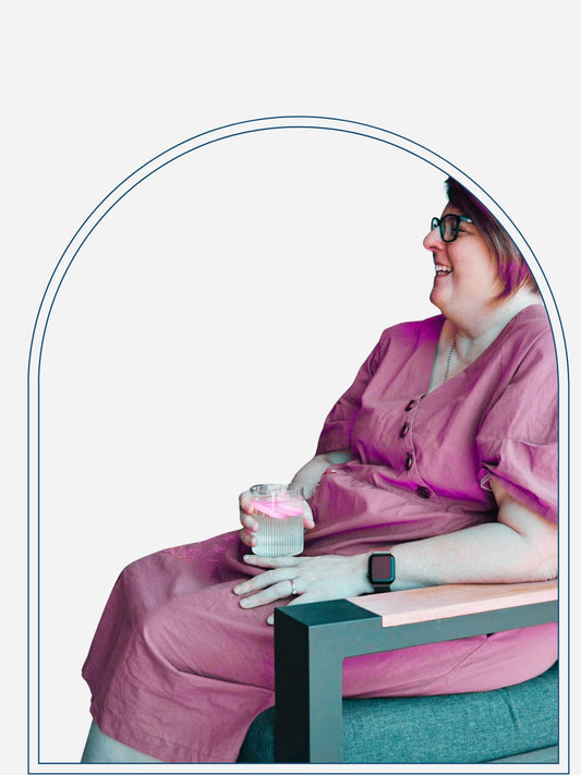 A person wearing a khaki stonewashed cotton dress with puff sleeves, sitting outdoors with a drink in their hand.