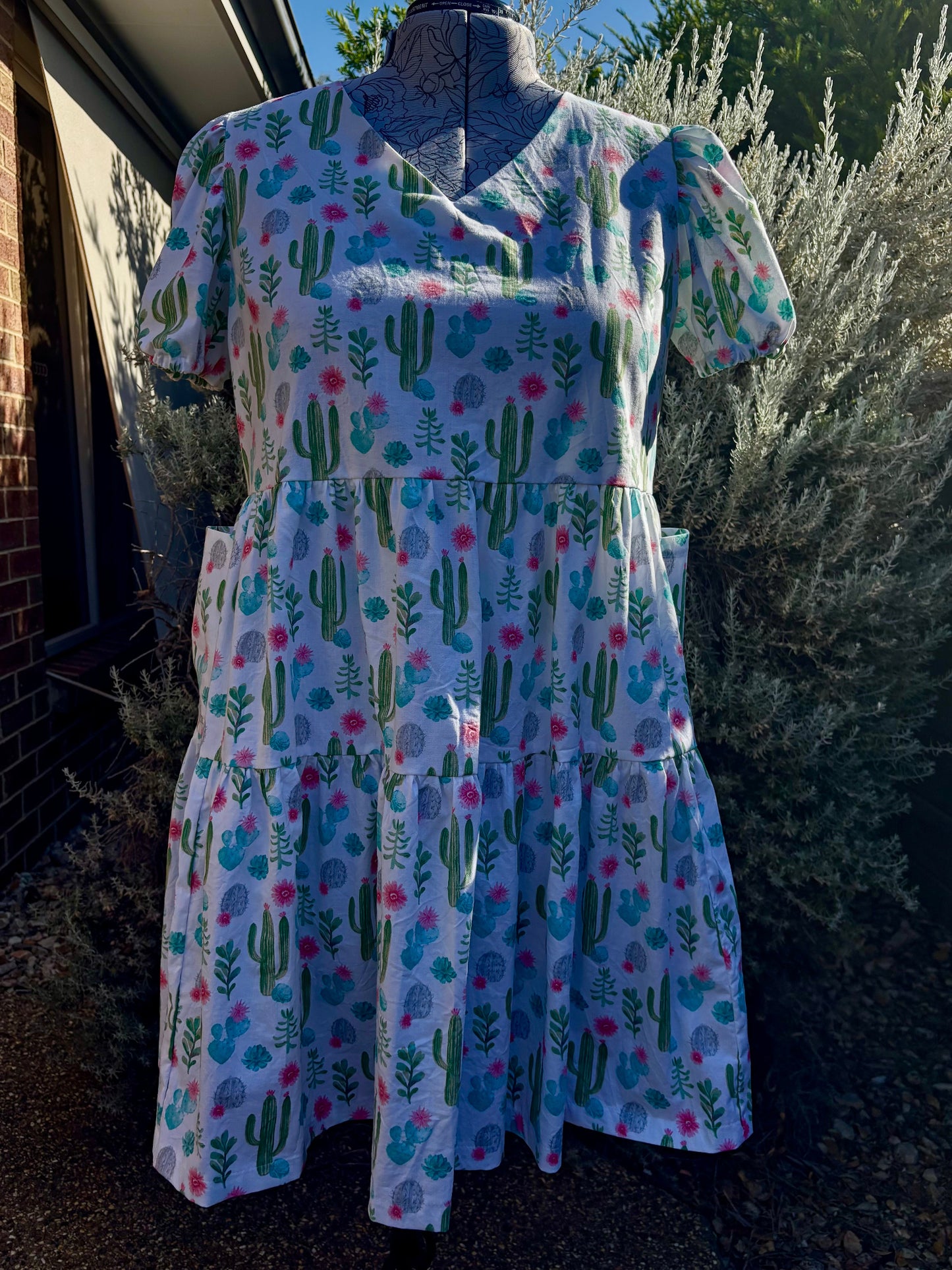 A cactus tiered dress displayed on a mannequin, with pockets, against an outdoor background.